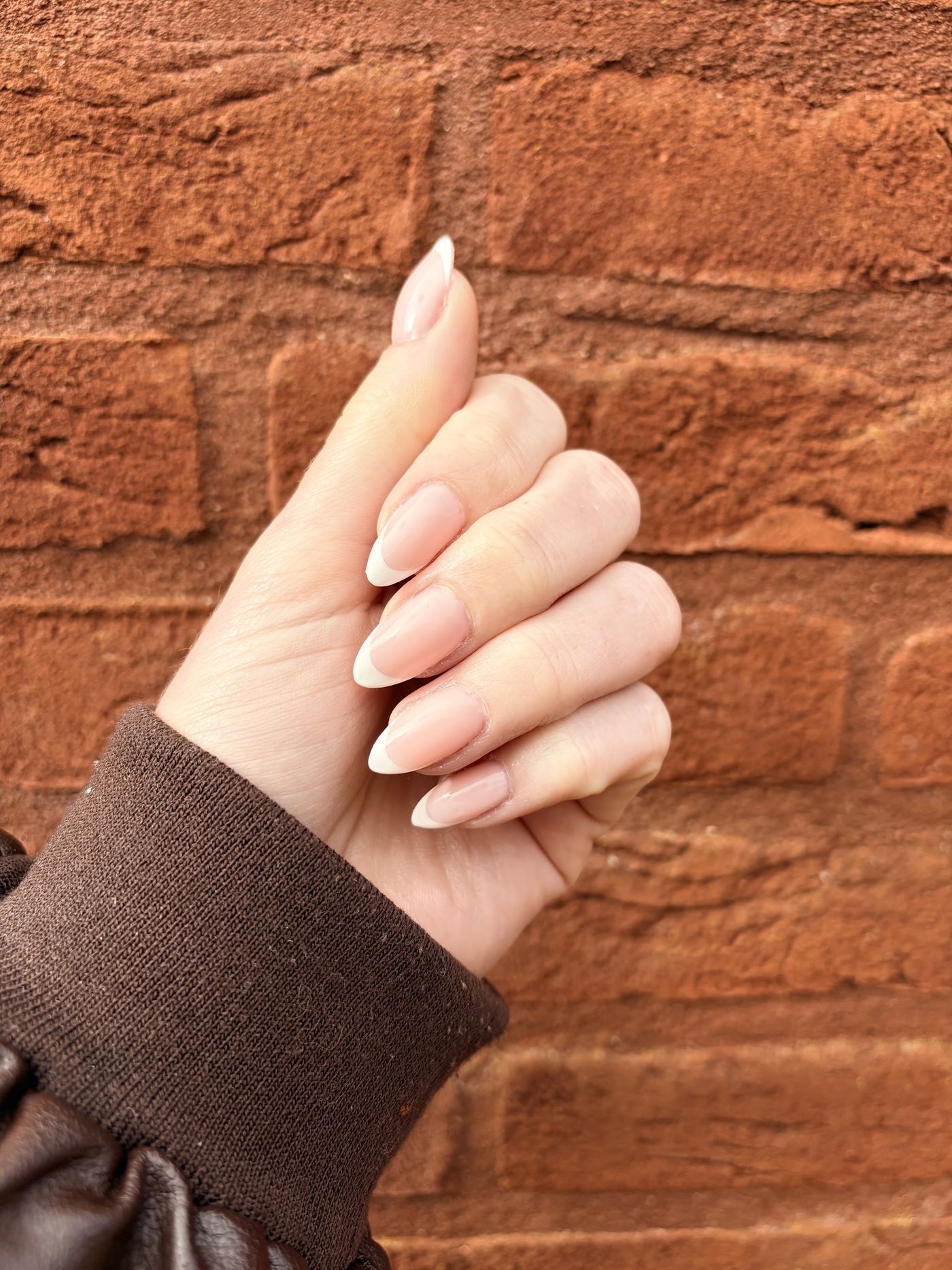 Naturelle amandelnagels tegen een bakstenen muur