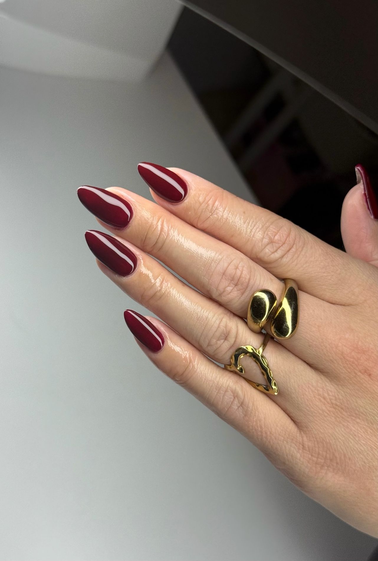 Glanzende diep bordeauxrode amandelnagels met gouden ringen